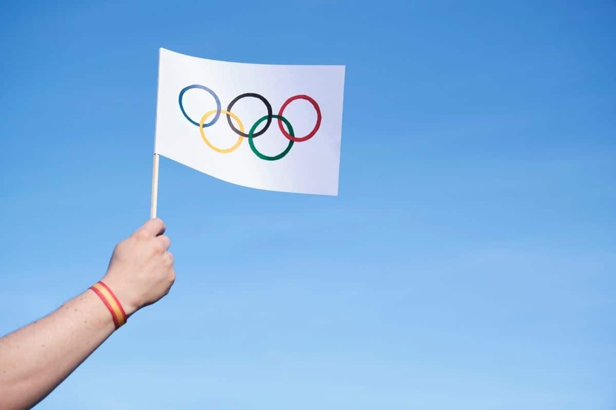 A hand holding the Olympic flag against a blue sky.