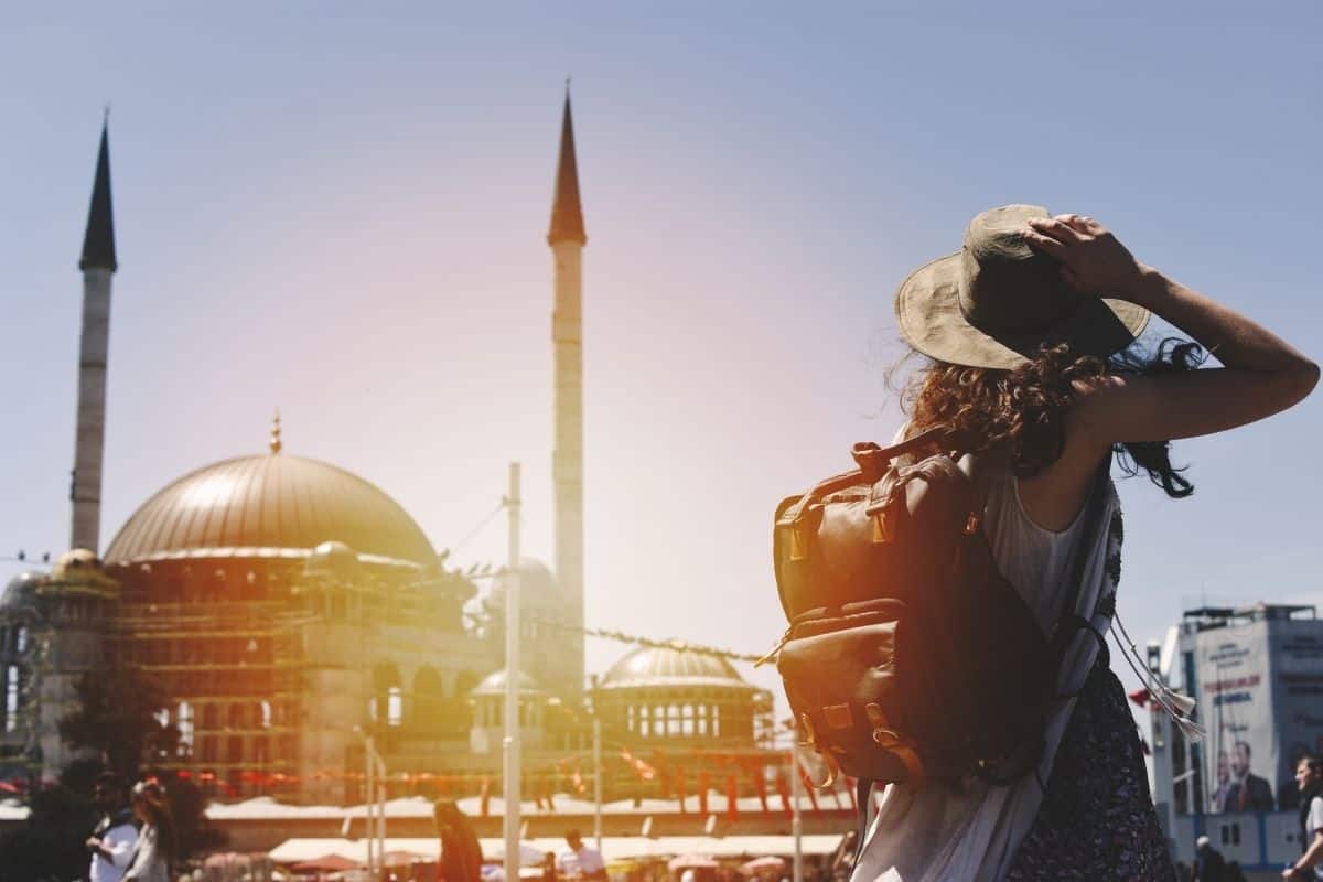 A tourist with a backpack and big hat looking at a mosque in Istanbul, Turkey.