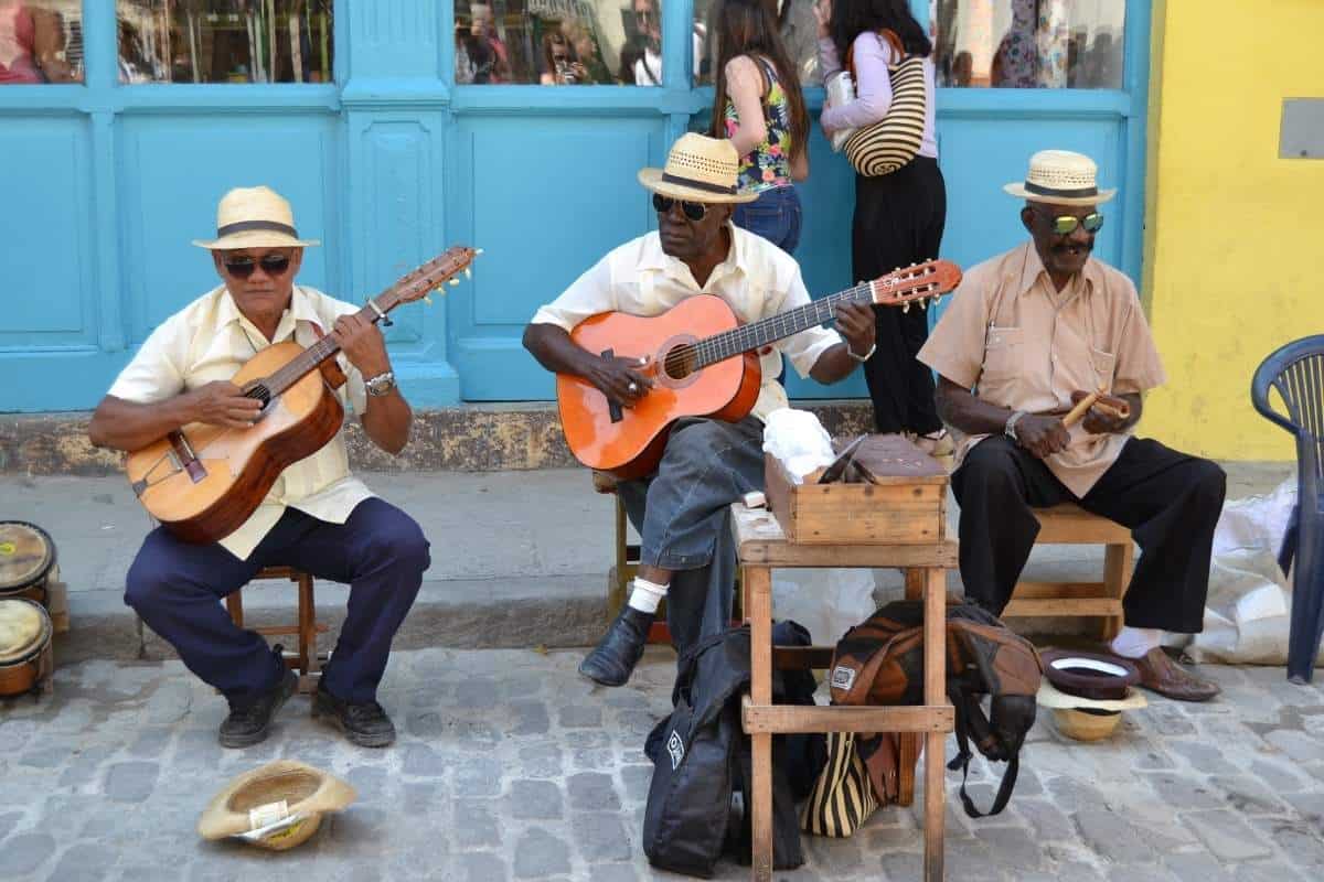 Three Cuban musicians wearing fedoras playing guitar on a cobblestone street