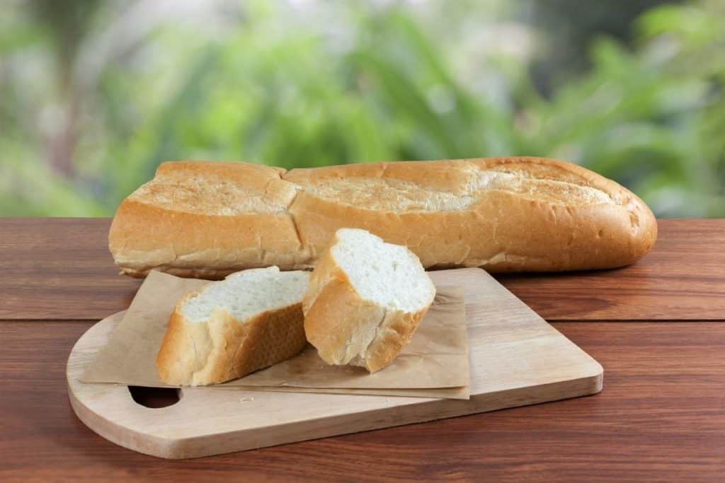French bread baguette cut on brown paper with a wooden board