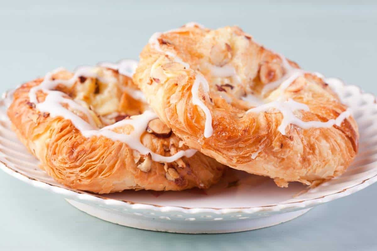 Two fresh Danish pastries with custard and almonds sitting on a plate