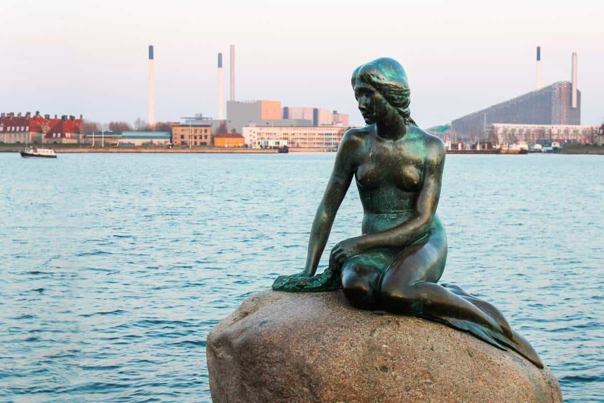 The famous mermaid statue along the water with Copenhagen in the background, Denmark