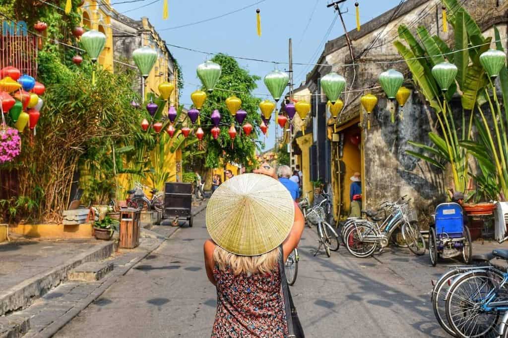 Woman in a straw hat taking a photo during the day on the streets of Vietnam