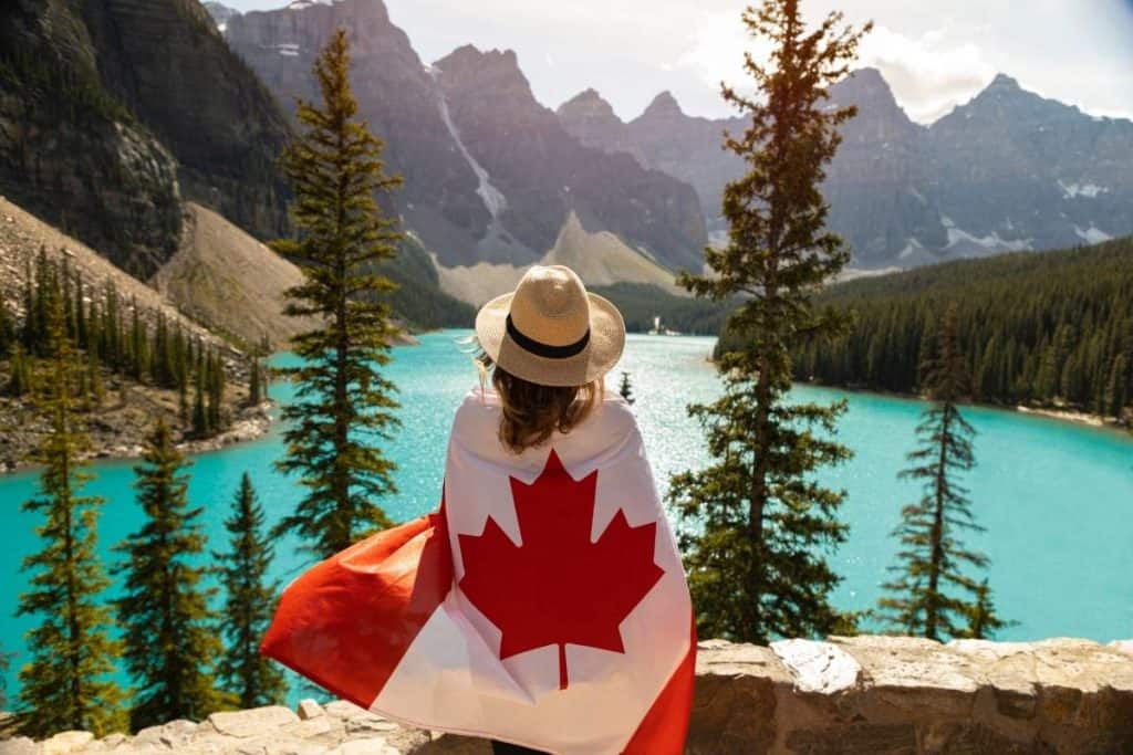 Women draped in Canada flag in front of Moraine Lake in Banff, Canada