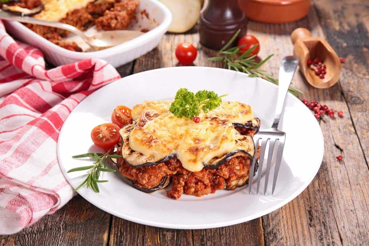 Moussaka, a Greek casserole made with eggplant, beef, and tomatoes, on a plate on a wooden table