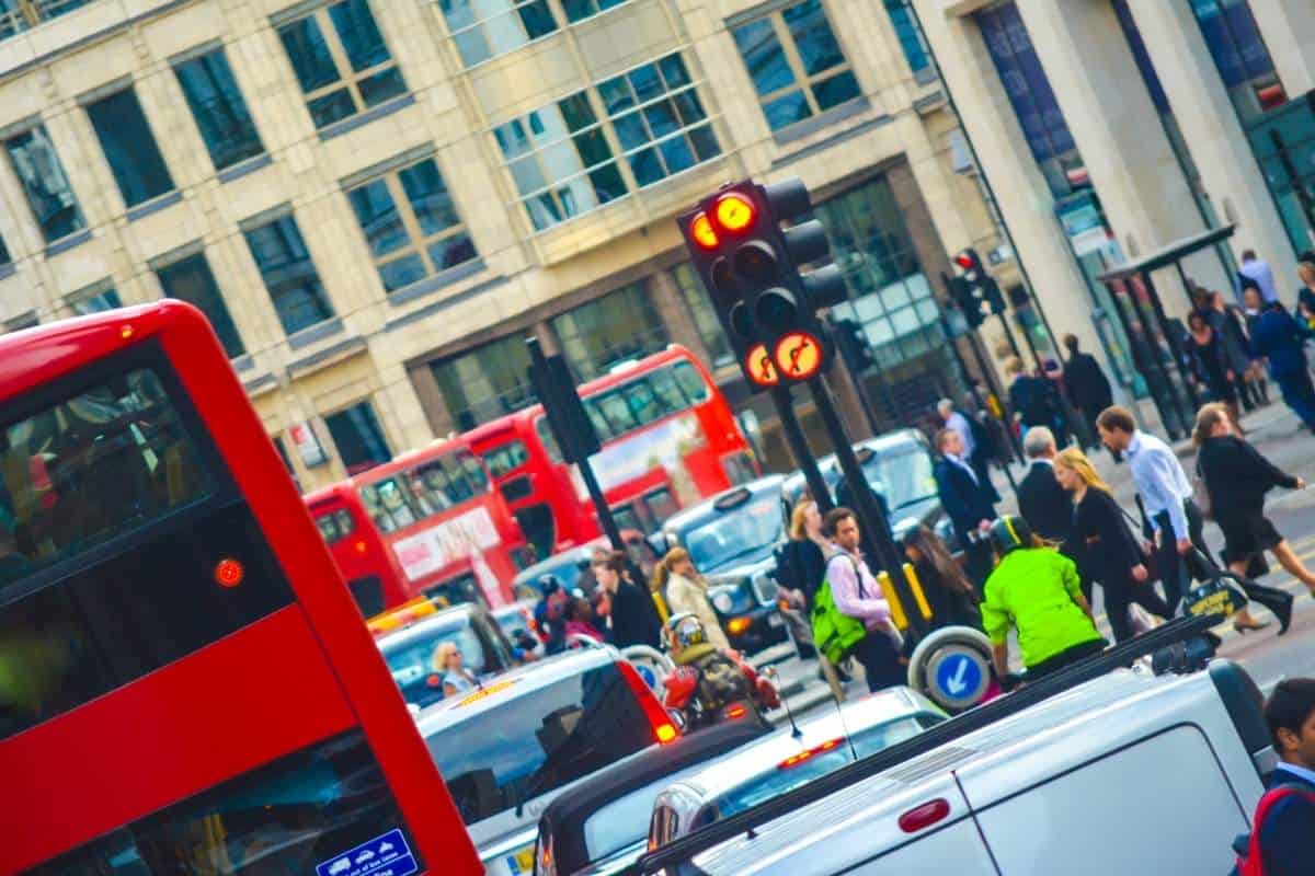 Busy street scene in London, England with red buses, cars driving, and people walking