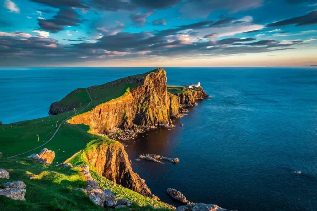Sweeping view of a sunset at Neist Point Lighthouse, Scotland with the ocean meeting the horizon in the distance