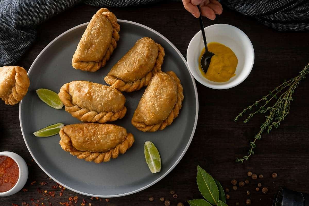 Aerial image of five empanadas on a grey plate with various sauces in dishes around them on a wood background
