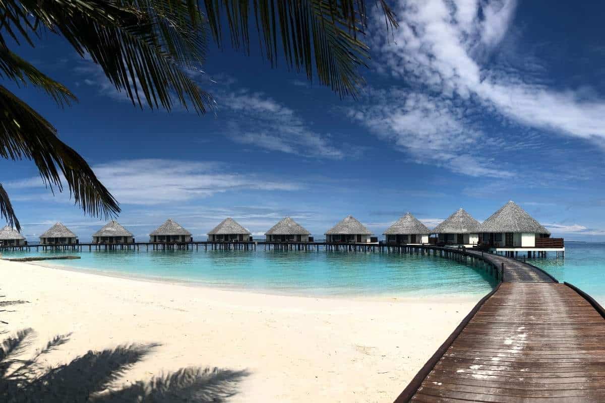 Boardwalk leading to a row of water villas on a resort island in the Maldives with white sand and blue skies