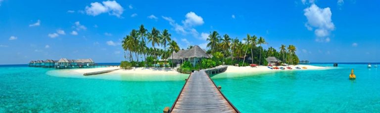 Boardwalk over top clear blue water leading to a straw hut on an island in the Maldives