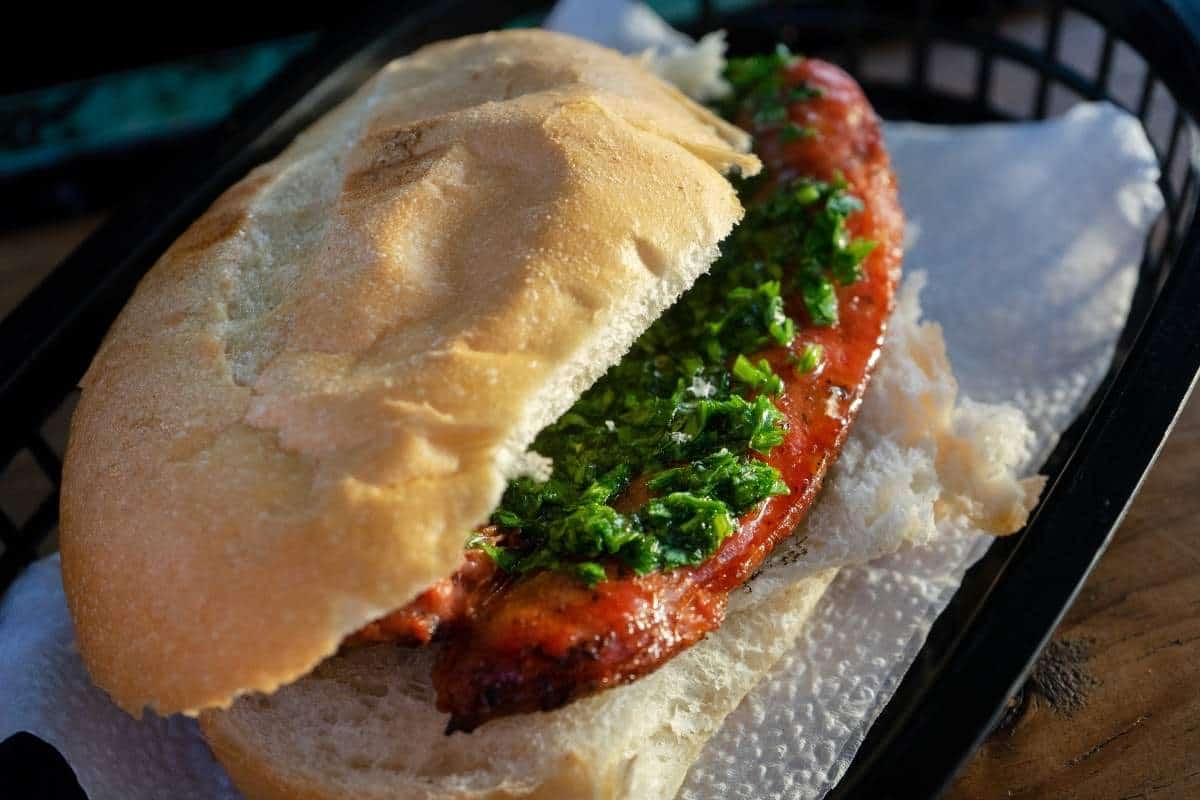 Close up view of Argentinian street food, choripan, featuring a chorizo sausage inside a crusty roll with green chimichurri sauce 