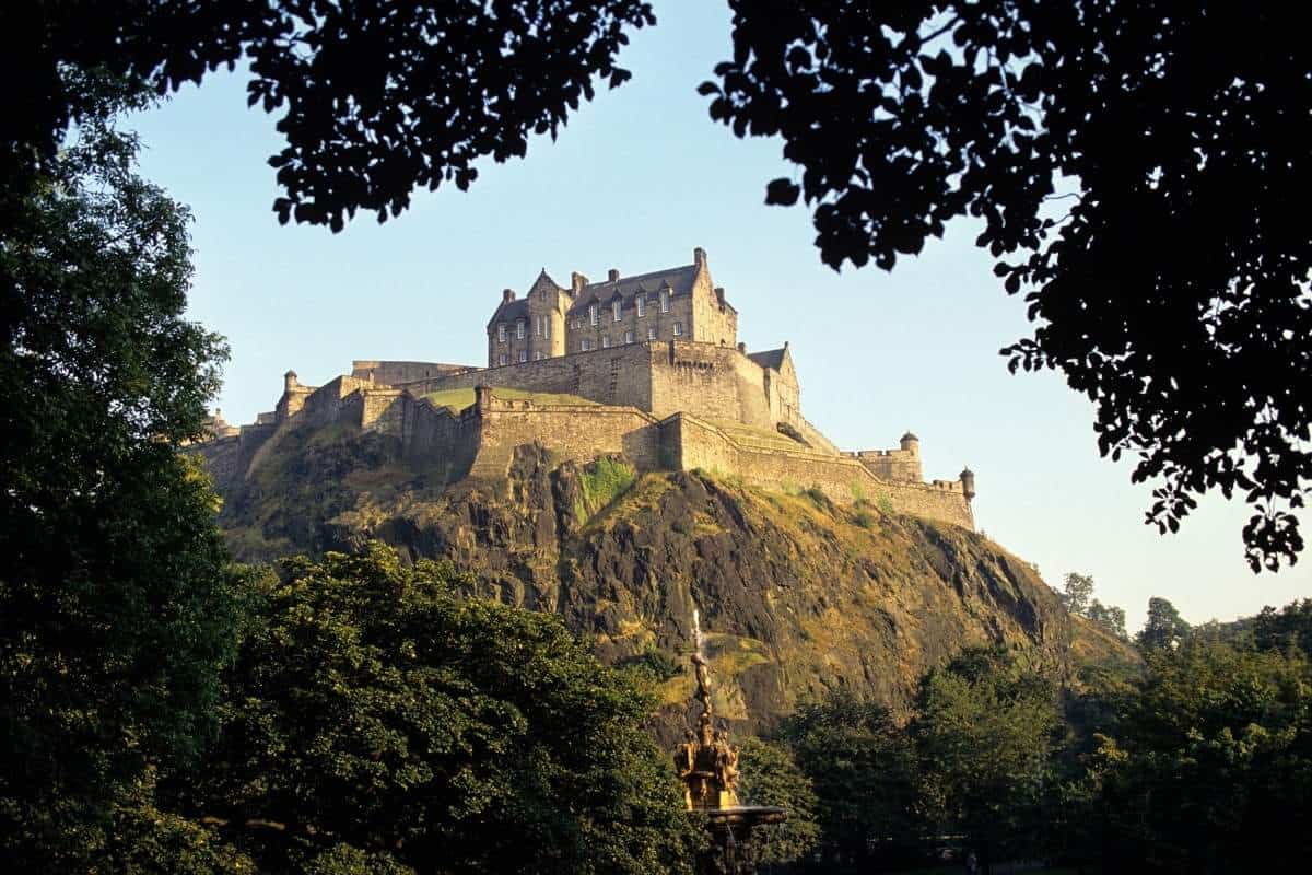 Edinburgh Castle illuminated by summer evening sunshine seen with tree leaves in the foreground