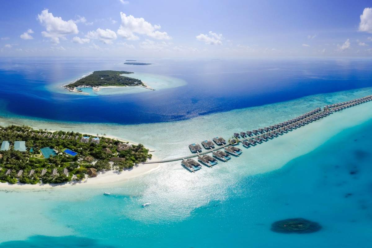Aerial view of a resort on a sandbar in the Maldives with clear blue water and blue sky in the horizon