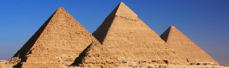 Full view of the three famous pyramids of Egypt with a deep blue sky behind them