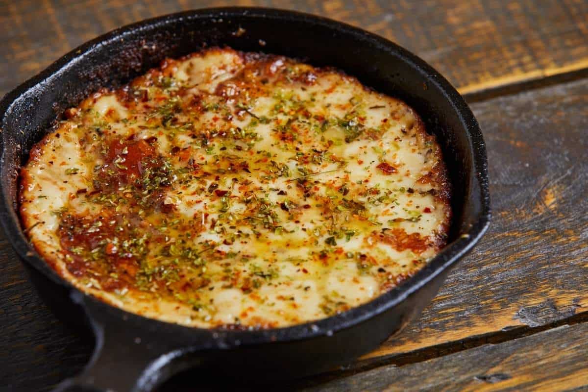 Bird eye view of provoleta, a baked cheese dish from Argentina, hot out of the oven and topped with herbs in a cast iron pan on a wooden table