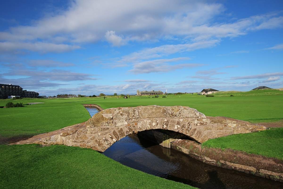 A cobblestone bridge arching over a stream on a golf course green