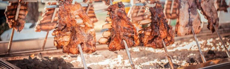 Landscape view of racks of meat skewered in a row being barbequed during an Argentinian asado