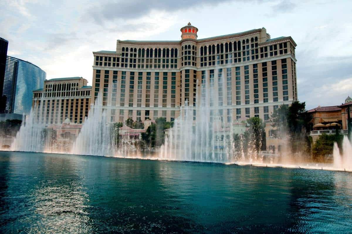 Bursts of water shooting up into the air in front of a large resort in Las Vegas with a cloudy sky in the background