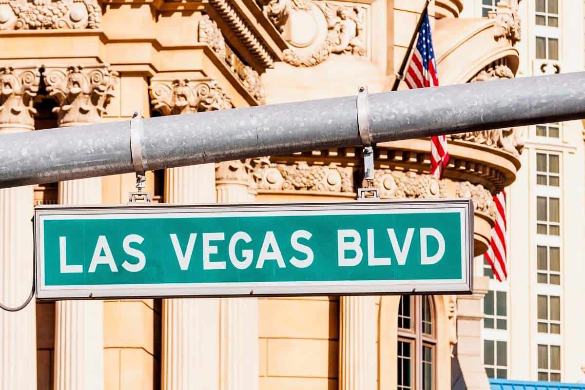 Green road sign that says Las Vegas Boulevard hanging from a grey pole with building columns in the background