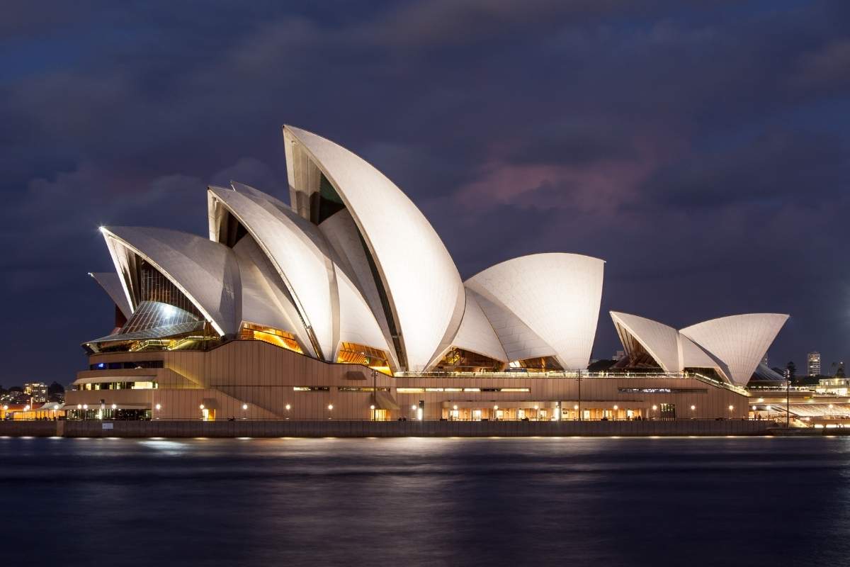 Sydney Opera House, one of the most famous world landmarks lit up at dusk with a dark sky and dark water surrounding the structure