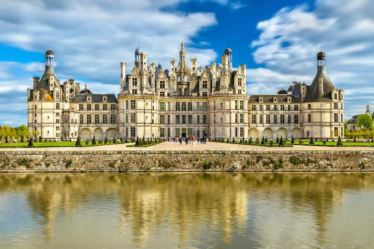 The remarkable structure of Chateau De Chambord with a lake reflecting its image in the foreground and a blue sky with white fluffy skies in the background