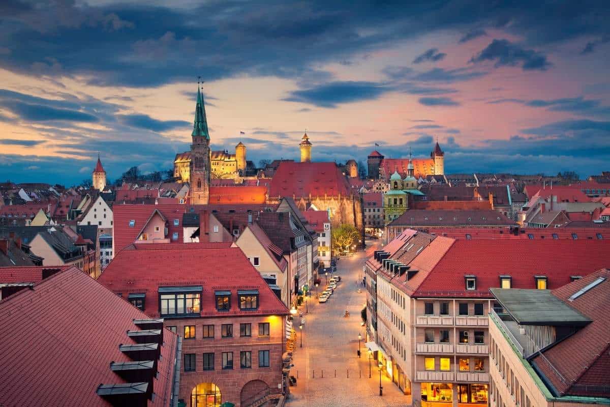 Aerial cityscape of the historic downtown of Nuremberg, Germany with an imposing castle in the distance and the sky a mix of blue, purple, and pink