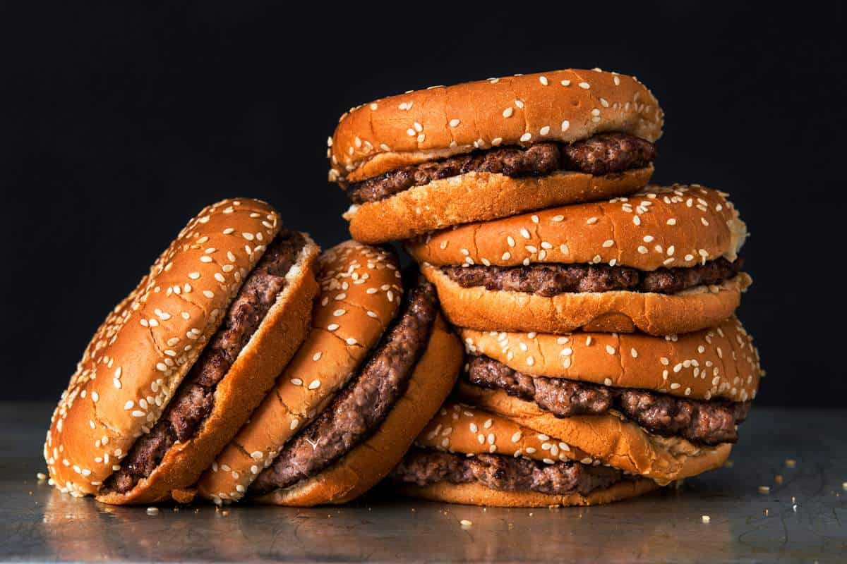 Five hamburgers divided into two stacks leaning on each other on a concrete slab with a black background