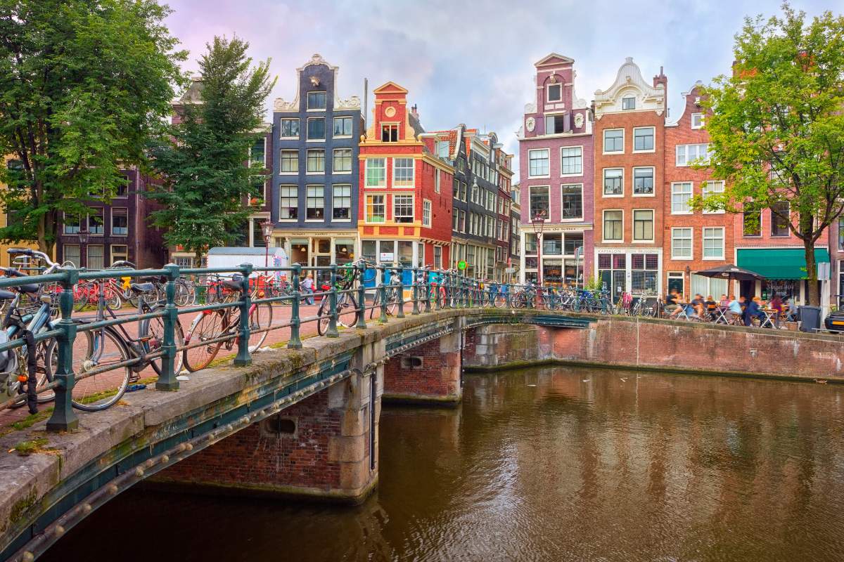Concrete bridge over a canal with bicycles along it leading to colorful houses 
