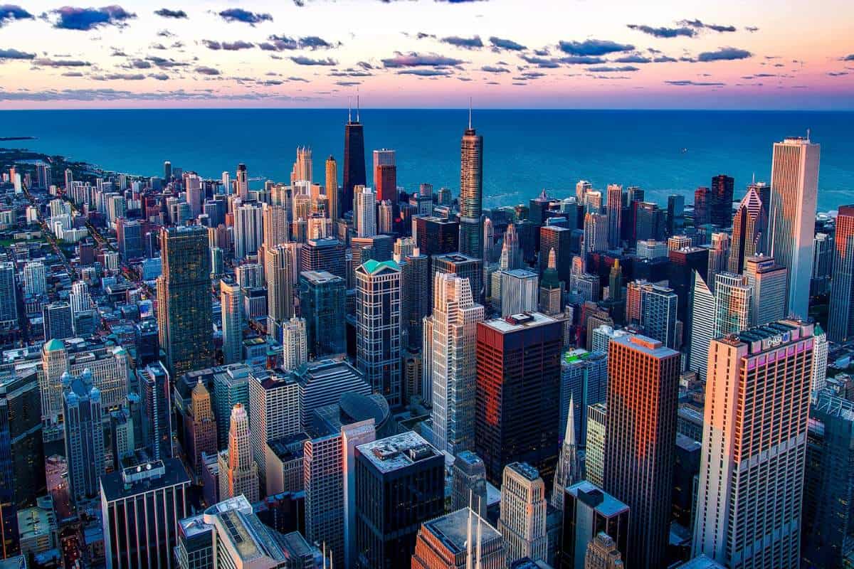 A cluster of skyscrapers along Lake Michigan at the beginning of sunset with just a strip of pink showing in the sky