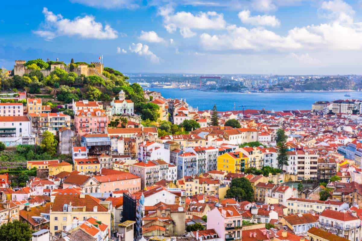 Town skyline of Lisbon, Portugal with a cluster of buildings and a castle overlooking them and the blue ocean