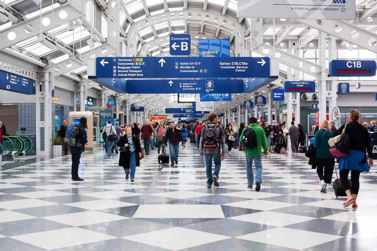 Passengers walking through O'Hare International Airport against a grey and white checkered tile floor and blue signage above