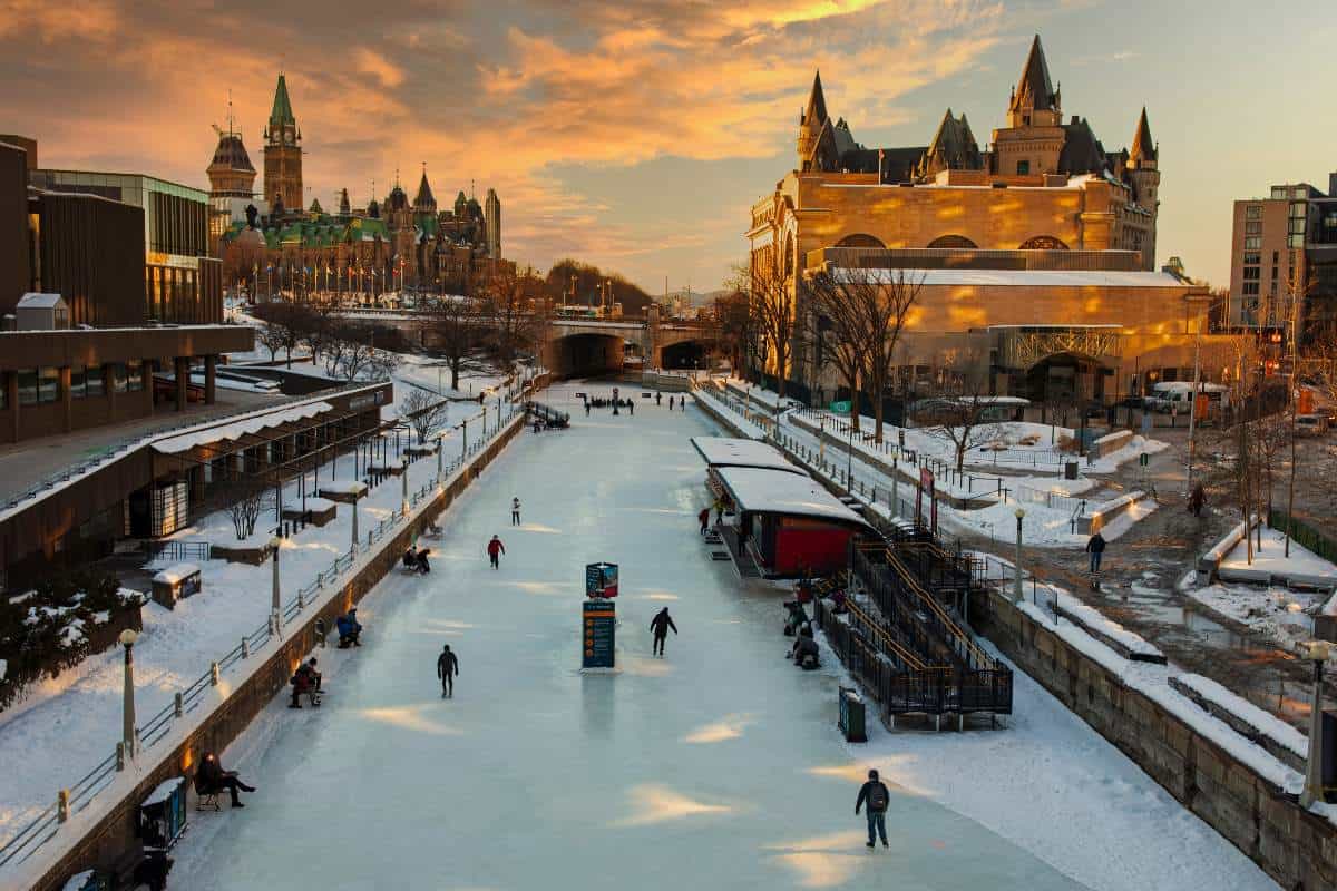 People skating on a frozen canal in Ottawa with the Canadian Parliament building in the background and the colors of the setting sun 