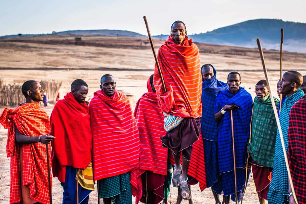 A row of African men wearing colorful scarves standing in a line holding wooden sticks