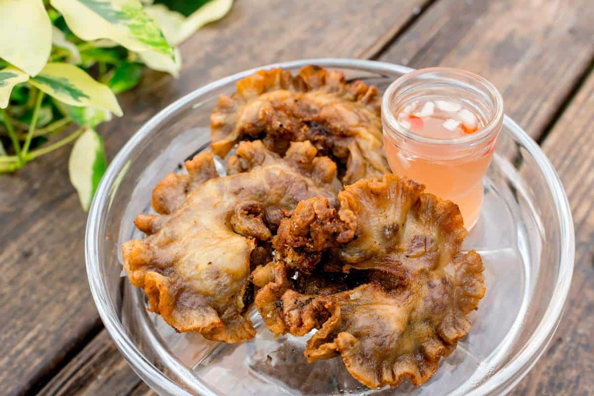 A plate of deep fried intestines on a glass plate with a side of spicy vinegar on a wooden table