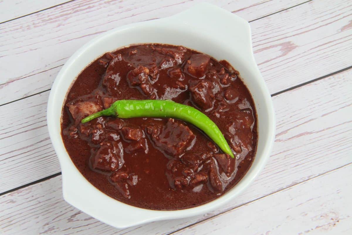 Top down perspective of a bowl of stew inside a white ceramic bowl topped with a green hot pepper