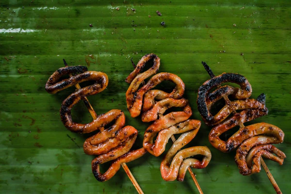 Closeup of three skewers of grilled pork intestines (isaw) on a green banana leaf - another one of the exotic foods in the Philippines