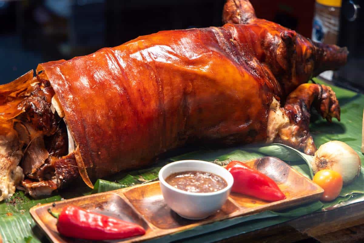 A whole barbecued pig presented on a table with condiments arranged on a wooden platter