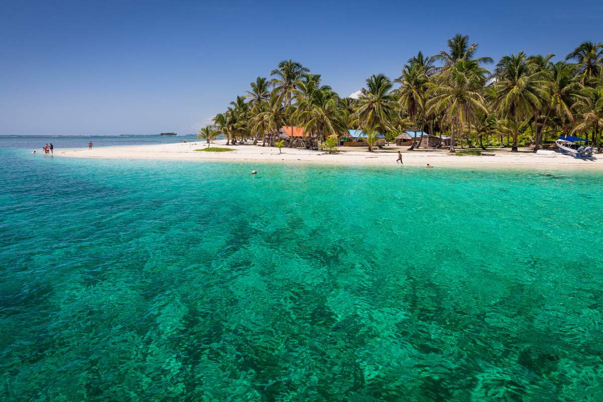 A remote beach in Panama with turquoise water, white sand, and palm trees on a blue skied day