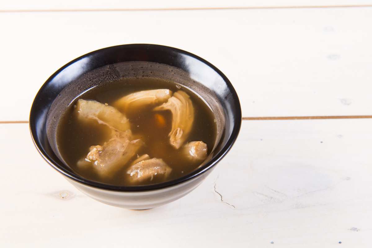 A black bowl of broth with questionable pieces floating in it on a white background