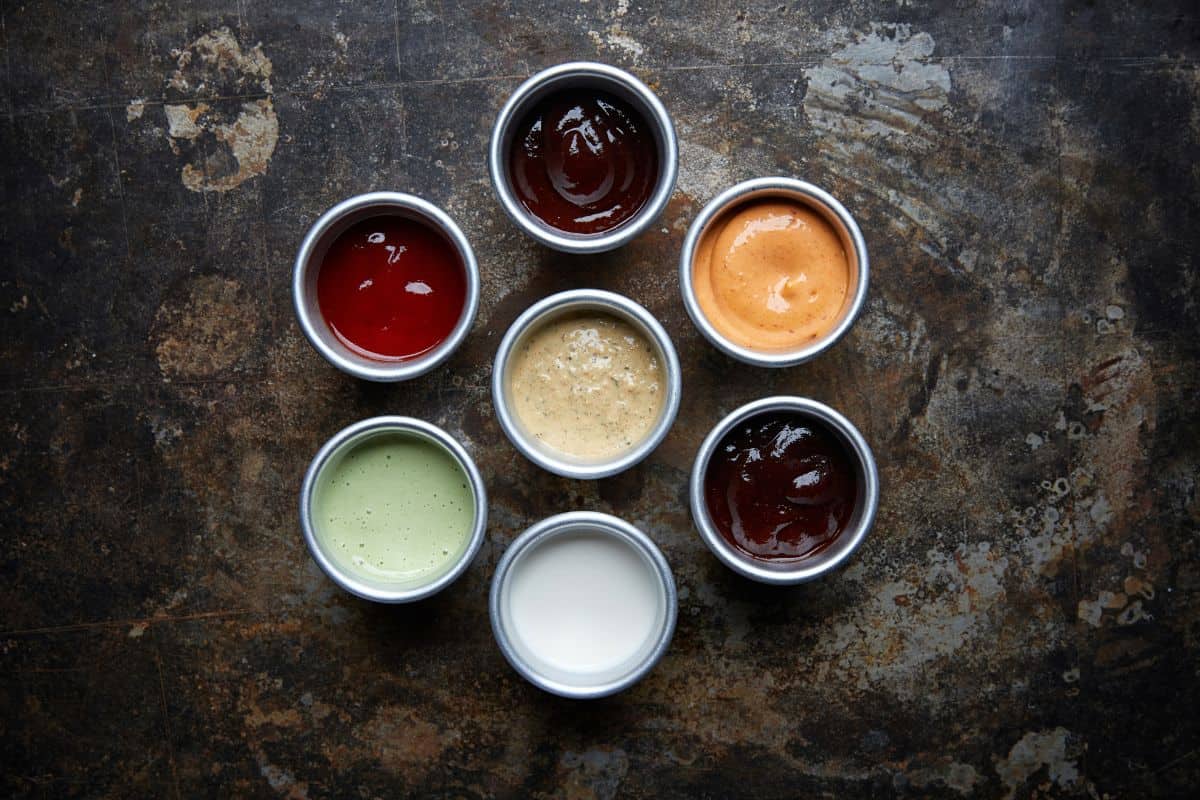 A selection of various dipping sauces in white bowls on a dark concrete background