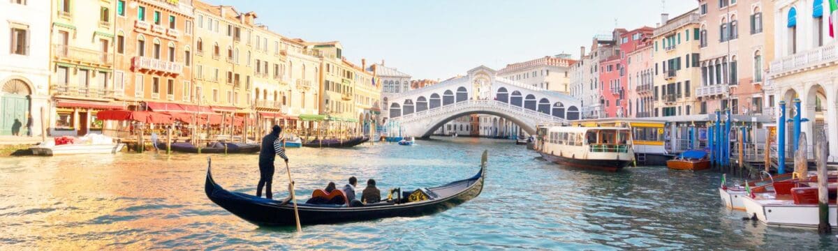 A gondola on the canals in Venice approaching a bridge with the water surrounded by colorful buildings