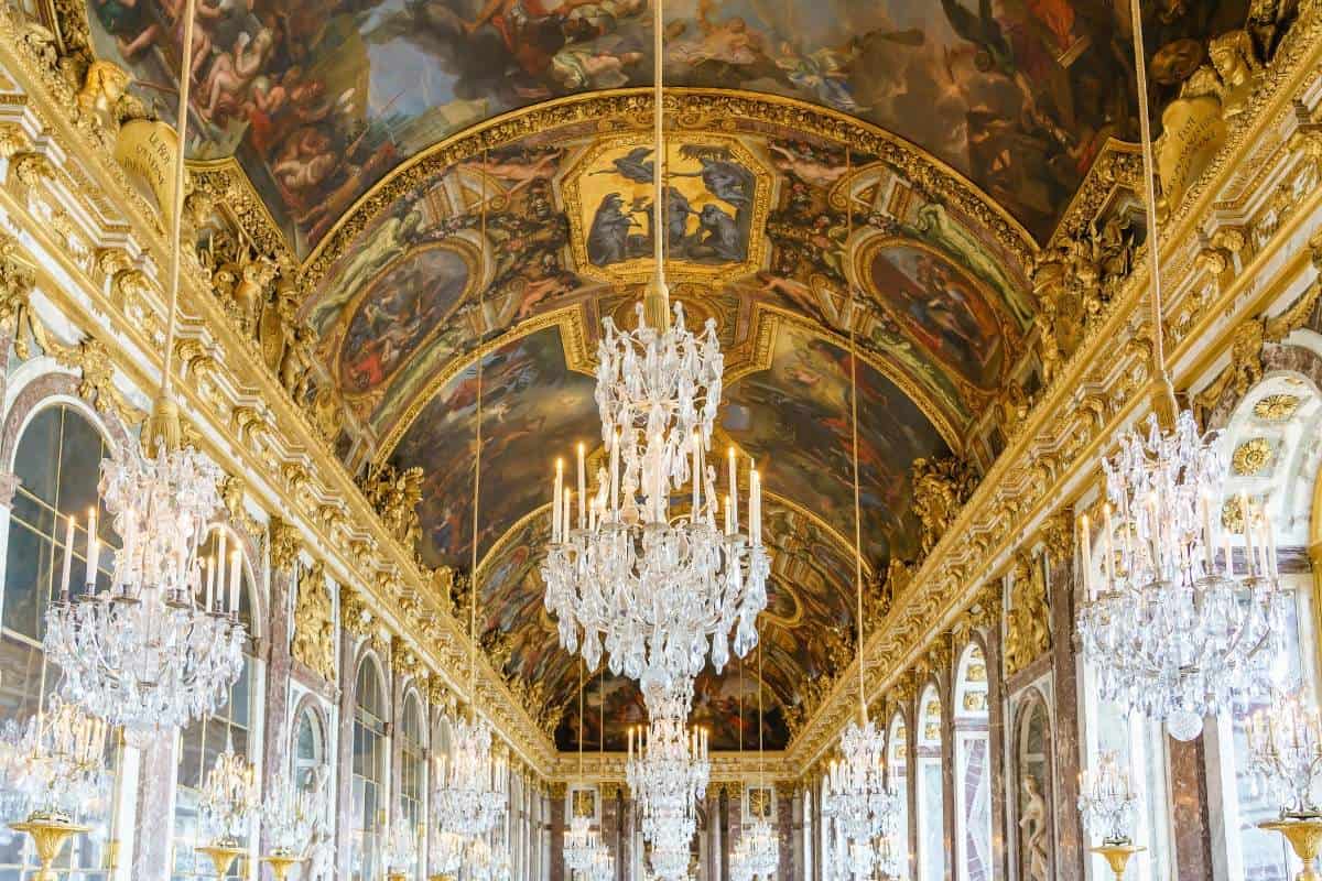 Interior shot of an opulent palace hallway with an intricately painted ceiling, crystal chandeliers, and large mirrors