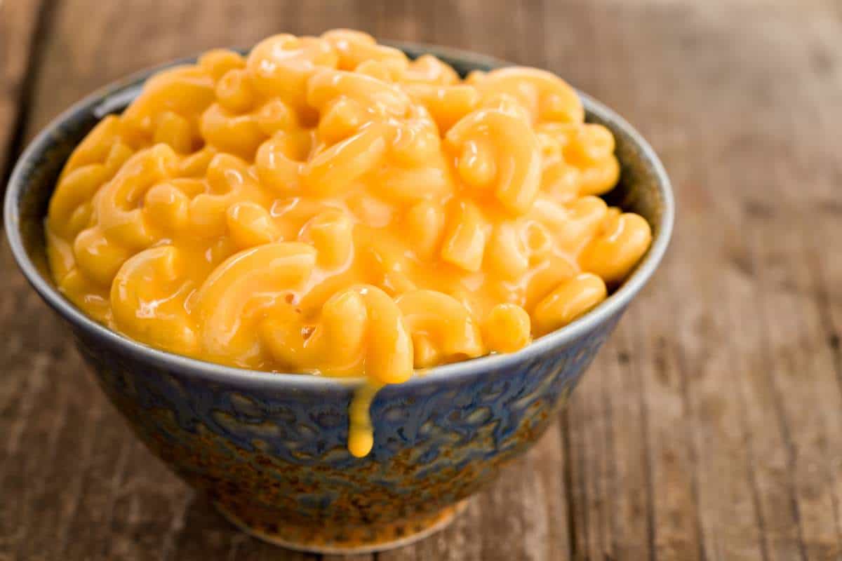 Extreme close up of a blue bowl full of creamy macaroni and cheese sitting on a wood table. 60+ Facts about US states